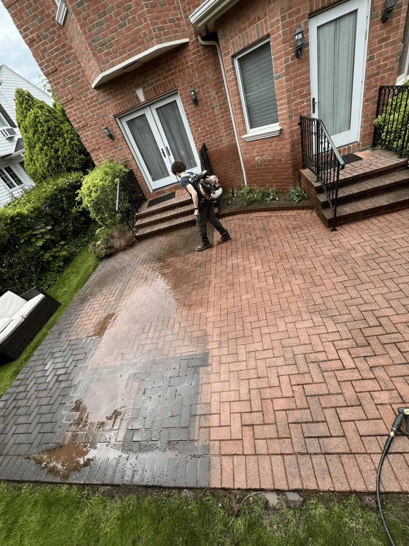 A brick patio being washed. The lower left section has not been washed yet and looks dull and grey, while the upper right brick has been washed and shows its original red colour.
