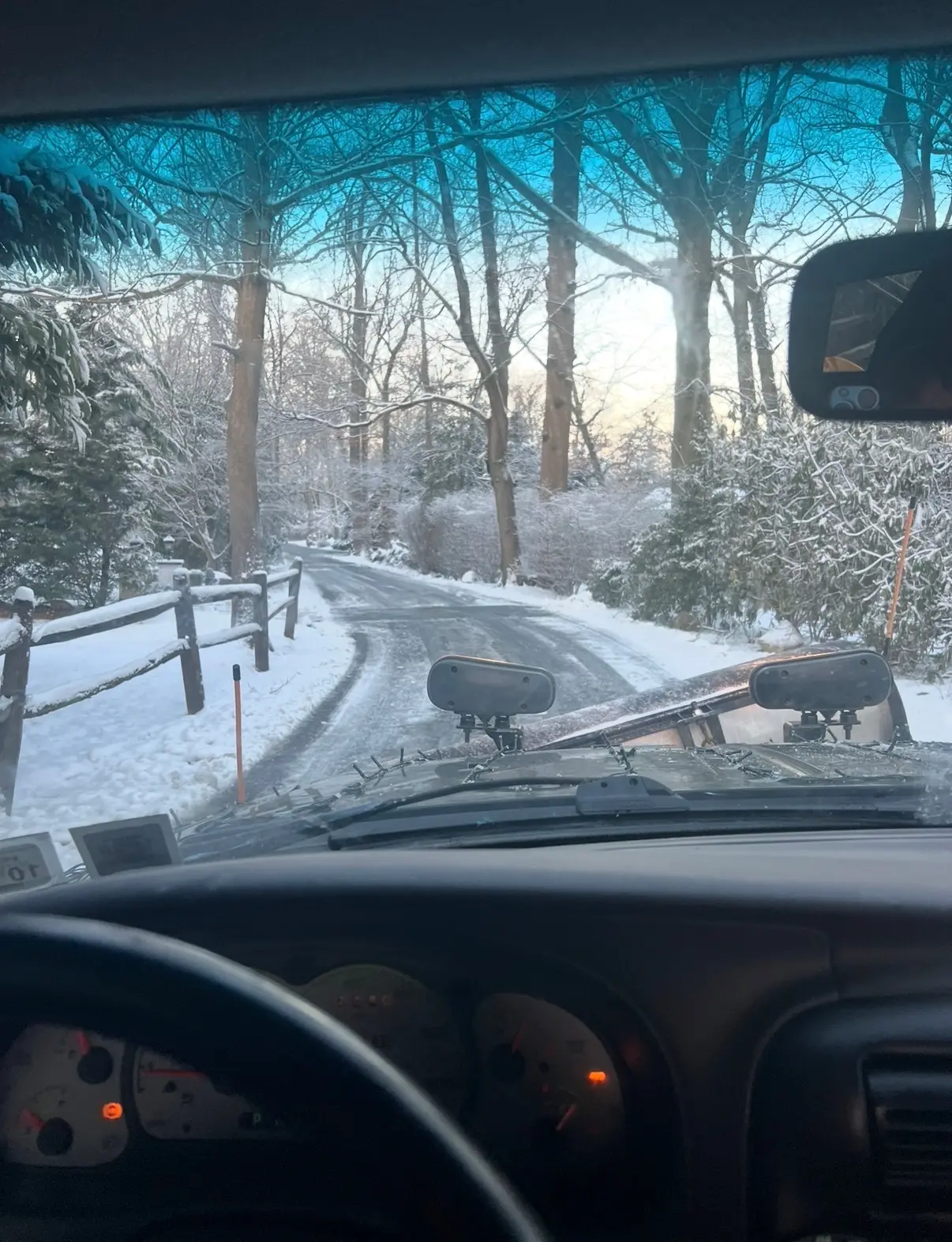 View through the windshield of a plow truck on a snow covered road lined with bare trees